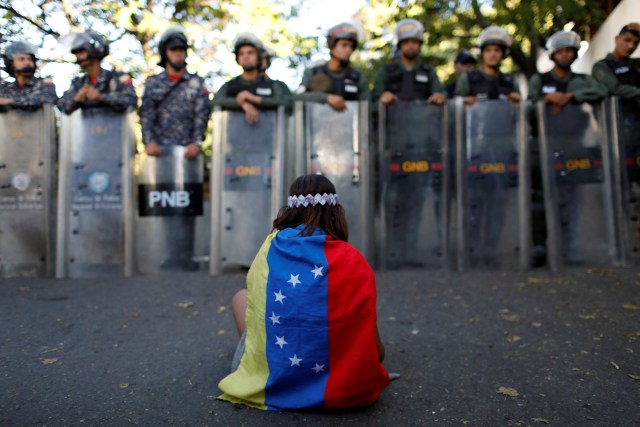 Una niña usa una bandera venezolana mientras las fuerzas de seguridad venezolanas bloquean el acceso a los partidarios de la oposición a la morgue principal de la ciudad, en Caracas, Venezuela. REUTERS/Marco Bello