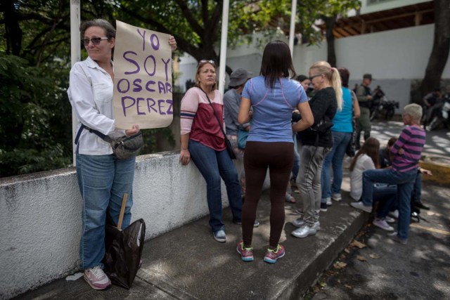 CAR11. CARACAS (VENEZUELA), 17/01/2018.- Una mujer (i) sostiene un cartel en el que se lee "Yo soy Óscar Pérez" frente a miembros de la Guardia Nacional Bolivariana y la Policía Nacional Bolivariana que custodian las inmediaciones de la morgue en donde está cuerpo del exagente Pérez hoy, miércoles 17 de enero de 2018, en Caracas (Venezuela). Decenas de agentes de la Policía Nacional Bolivariana custodian desde la mañana de hoy los alrededores de la principal morgue de Caracas, después de que familiares de Óscar Pérez, el exagente alzado contra el Gobierno chavista quien falleció el lunes, exigieran identificar su cuerpo. EFE/MIGUEL GUTIÉRREZ