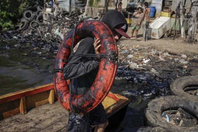 En Cabimas, un hombre carga un salvavidas cubierto de petróleo extraído del lago de Maracaibo. Después de regresar del lago, los pescadores se empapan de gasolina para limpiar el petróleo empapado de sus cuerpos.