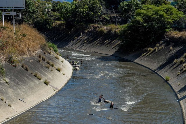 Los hombres buscan metales valiosos en un canal de aguas residuales en el río Guaire, en Caracas, el 1 de febrero de 2018. Decenas de jóvenes buscan diariamente joyas perdidas en el río Guaire, donde drenan las alcantarillas de Caracas. Encontrar oro es su ilusión, pero una pieza de alambre de cobre es suficiente para paliar el hambre. / AFP PHOTO / FEDERICO PARRA