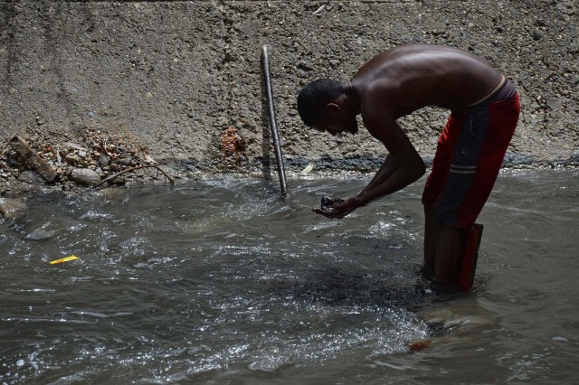 Un hombre saca barro del fondo de un canal de alcantarillado mientras busca metales valiosos en el río Guaire, en Caracas, el 1 de febrero de 2018. Decenas de jóvenes buscan diariamente joyas perdidas en el río Guaire, donde drenan las alcantarillas de Caracas. . Encontrar oro es su ilusión, pero una pieza de alambre de cobre es suficiente para paliar el hambre. / AFP PHOTO / FEDERICO PARRA