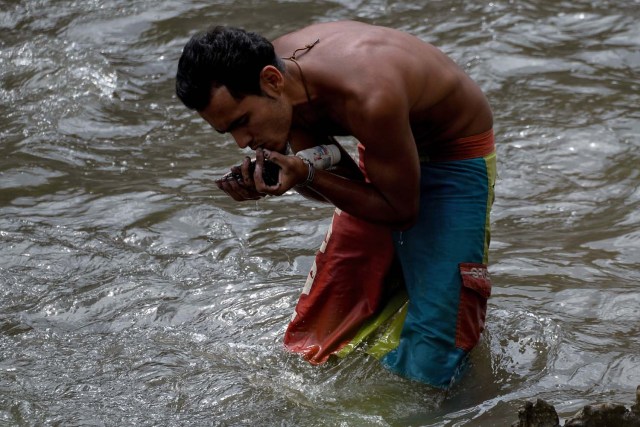 Un hombre saca barro del fondo de un canal de alcantarillado mientras busca metales valiosos en el río Guaire, en Caracas, el 1 de febrero de 2018. Decenas de jóvenes buscan diariamente joyas perdidas en el río Guaire, donde drenan las alcantarillas de Caracas. . Encontrar oro es su ilusión, pero una pieza de alambre de cobre es suficiente para paliar el hambre. / AFP PHOTO / FEDERICO PARRA