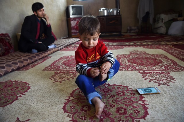 This picture taken on March 16, 2018 shows Afghan father Sayed Assadullah Pooya, 28, looking on alongside his son Donald Trump, aged around 18 months, during an interview with AFP at their home in Kabul. Donald Trump flops over his pink and white baby walker and rolls it around the unfurnished room in Kabul, blissfully unaware of the turmoil his "infidel" name is causing in the conservative Muslim country. The rosy-cheeked toddler, whose parents named him after the more famous Donald Trump in the hope of replicating his success, is at the centre of a social media firestorm after a photo of his Afghan ID papers was posted on Facebook. / AFP PHOTO / Wakil KOHSAR / TO GO WITH 'AFGHANISTAN-PEOPLE-RELIGION' BY ALLISON JACKSON AND MUSHTAQ MOJADDIDI