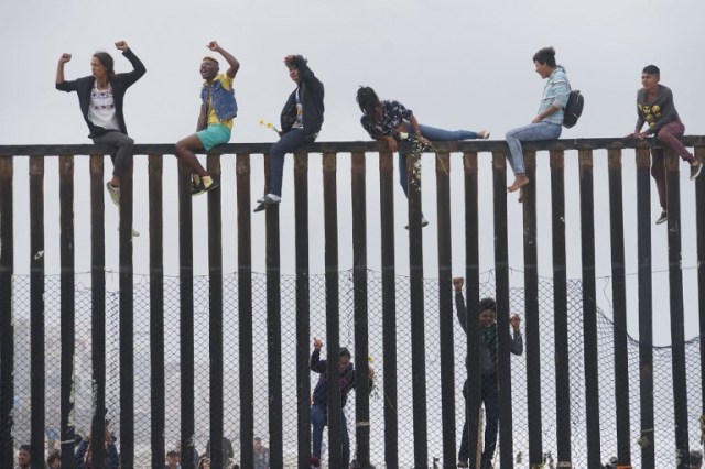 Manifestantes de caravanas migrantes suben la valla fronteriza entre Estados Unidos y México durante un mitin, el 29 de abril de 2018, en San Ysidro, California. Estados Unidos ha amenazado con arrestar a unos 100 migrantes centroamericanos si intentan colarse desde la frontera entre Estados Unidos y México donde se han reunido, lo que provocó que el presidente estadounidense Donald Trump ordene refuerzos de tropas en la frontera.  Sandy Huffaker / AFP