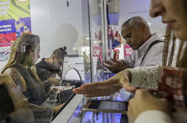 Venezuelan Carlos Figueroa (2R), transfers money to his family in Venezuela at a money transfer agency in Medellin, Colombia, on April 16, 2018. Exiled Venezuelans have no expectations of the presidential election taking place next May 20 in their home country. / AFP PHOTO / JOAQUIN SARMIENTO