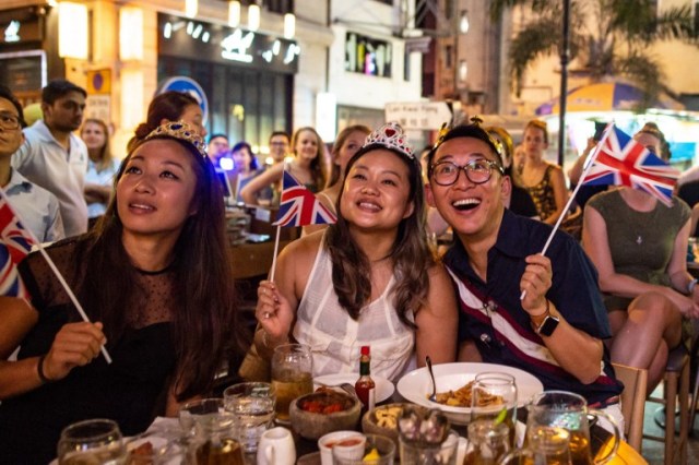 People attend a screening party at a bar showing the wedding ceremony of Britain's Prince Harry, Duke of Sussex and his wife Meghan, Duchess of Sussex in Windsor, in Hong Kong on May 19, 2018. / AFP PHOTO / Philip FONG